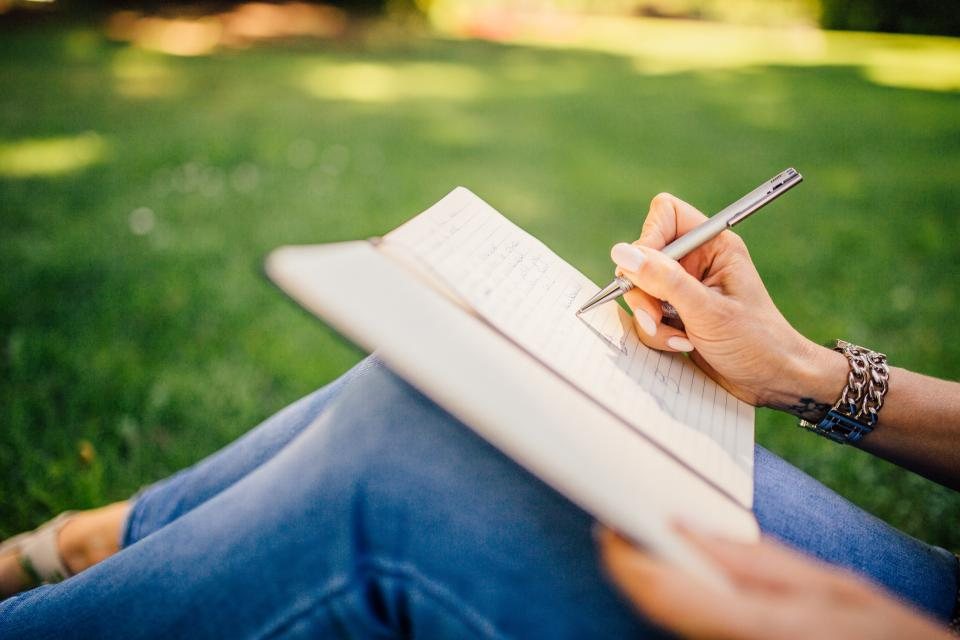 Person writing in a notebook while sitting on the grass